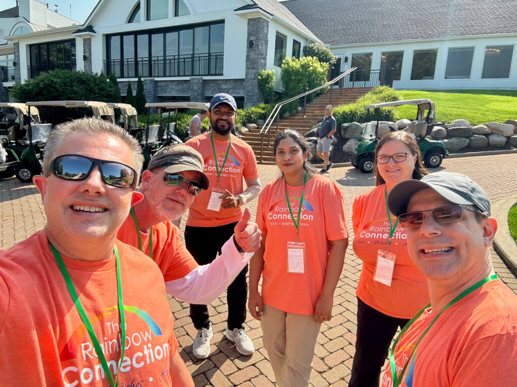 MOTOR employees volunteering at The Rainbow Connection charity golf event, smiling in orange event shirts with golf carts in the background.