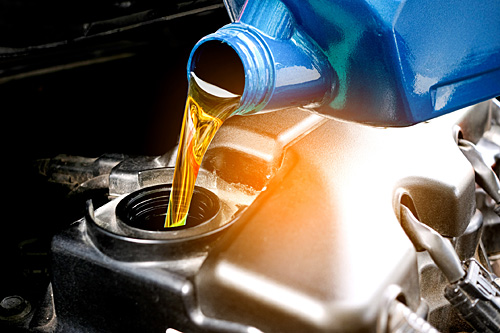 Close-up of motor oil being poured from an API-certified container into a vehicle engine, representing proper automotive maintenance and lubricant standards.