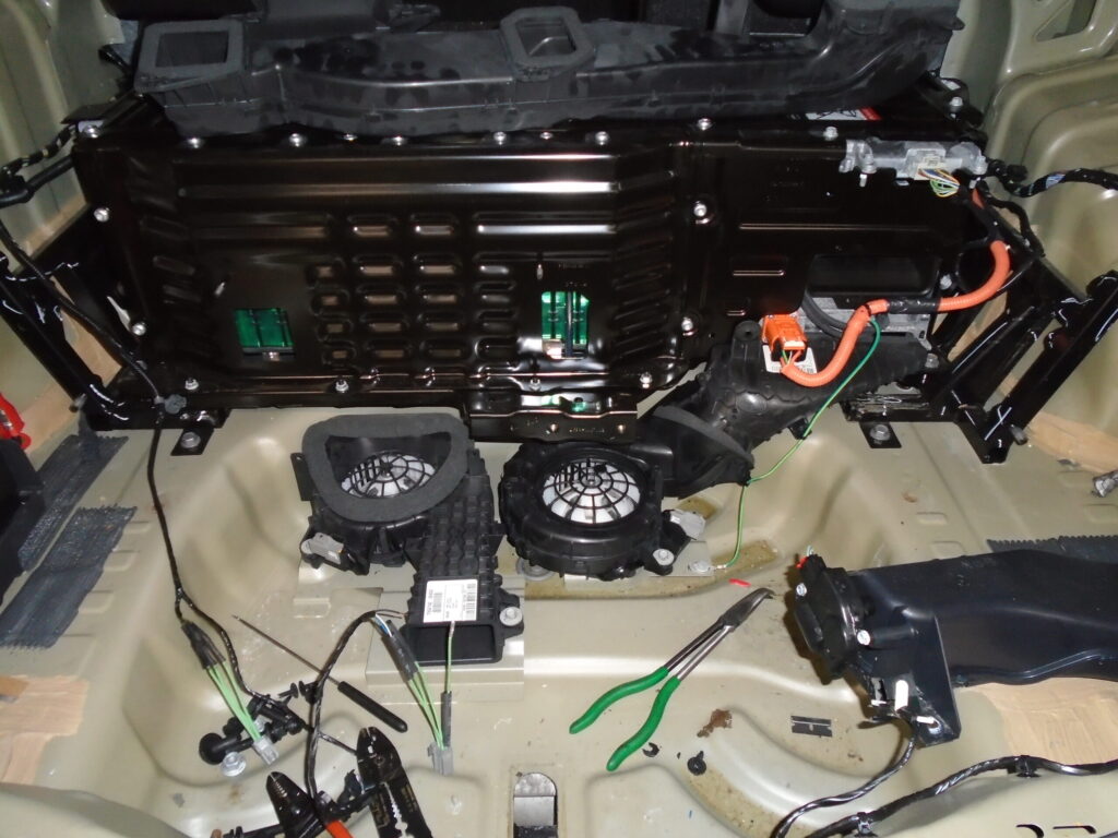 HV battery pack (HVBP) with dual cooling fans mounted in the spare tire well of a hybrid vehicle, showing vulnerability to water intrusion.