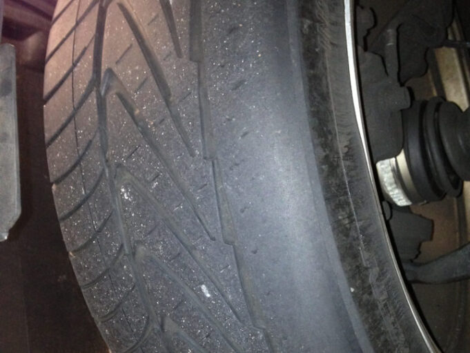 Close-up of a car tire with severe tread wear, showing bald spots and uneven surface indicating need for replacement.
