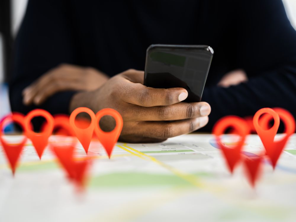 Close-up of a person using a smartphone over a paper map with multiple red location pins, symbolizing GPS navigation, mapping technology, and route planning.