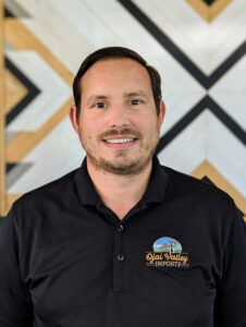 Patrick Rivera of LBM Automotive wearing a black Ojai Valley Imports polo shirt, smiling in front of a geometric wall design.