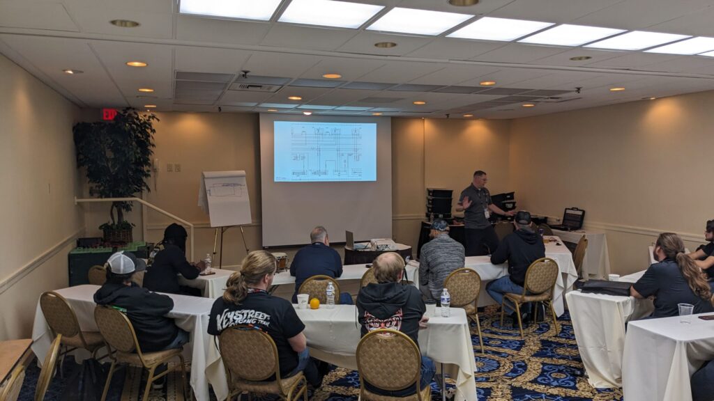 Instructor leading an automotive training session at Super Saturday 2025, presenting a wiring diagram to attendees seated in a classroom setting.