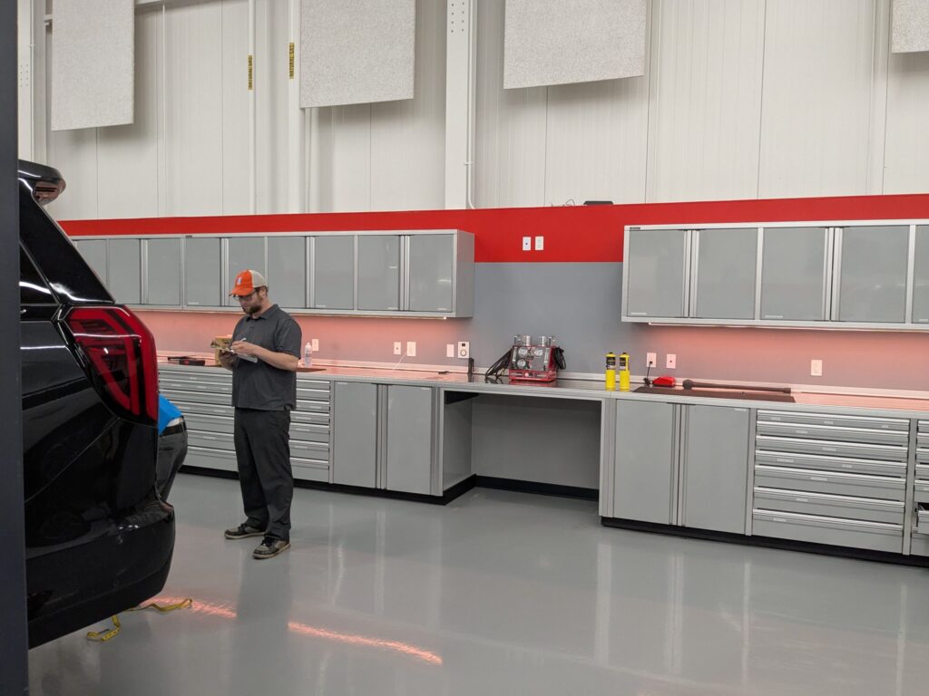 Technician reviewing notes on a clipboard beside a black SUV in a clean, well-equipped workshop with gray cabinets and a red accent wall.