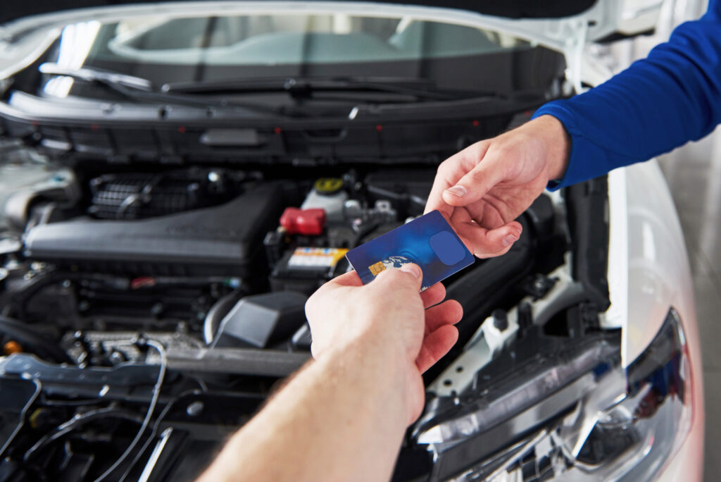 Hands of car mechanic with wrench in garage, payment by credit card.